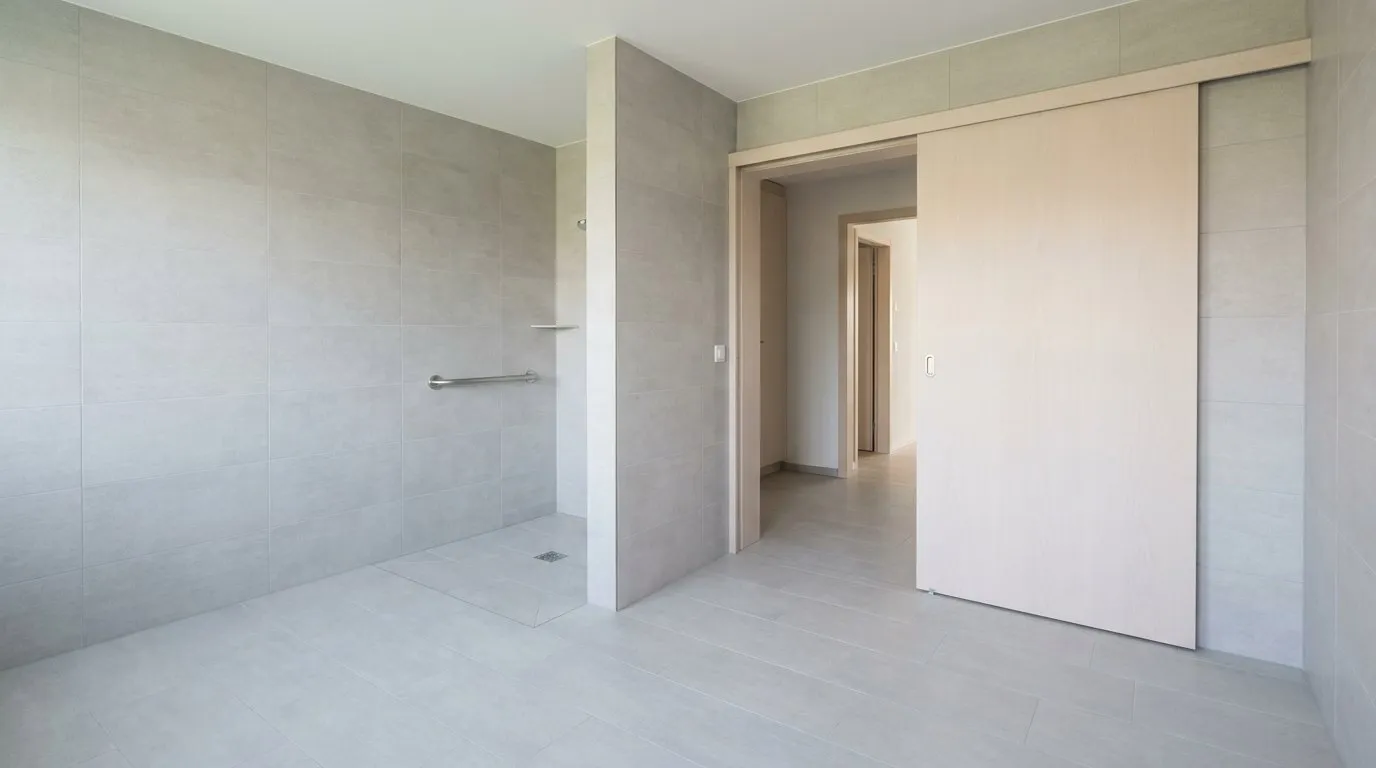 Salle de bains terminée avec douche de plain-pied sans ressaut, barre d'appui en inox et porte coulissante large.
